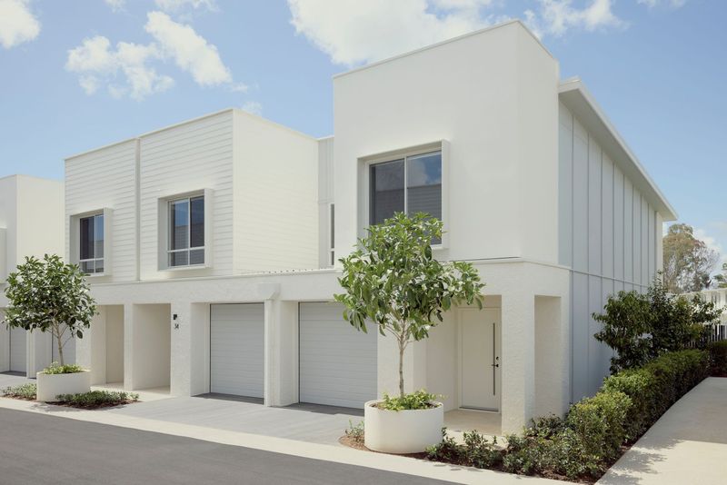 Elwood by Azure townhouses in Mango Hill, white rendered two-storey facades with garages and a potted tree