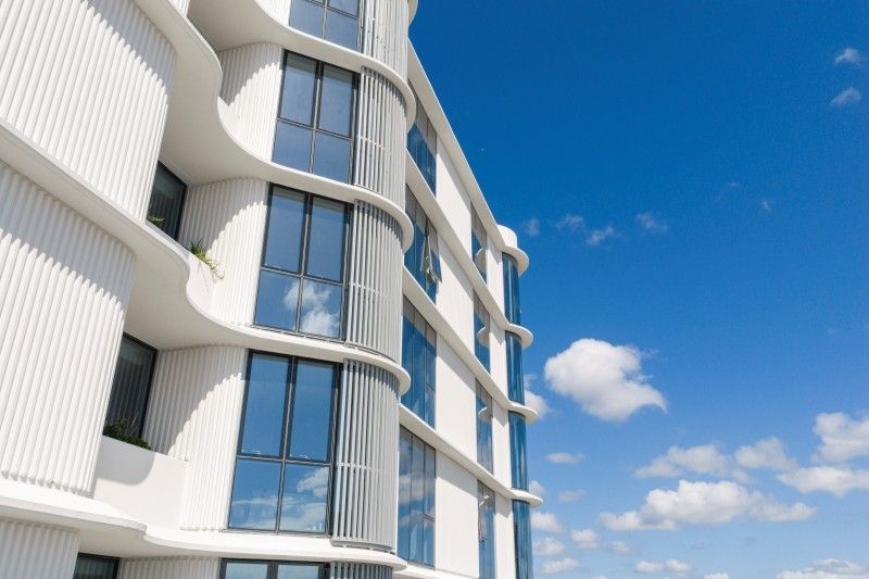 Curved white fluted facade and windows of Isabel by Mosaic in Burleigh Heads against a blue sky