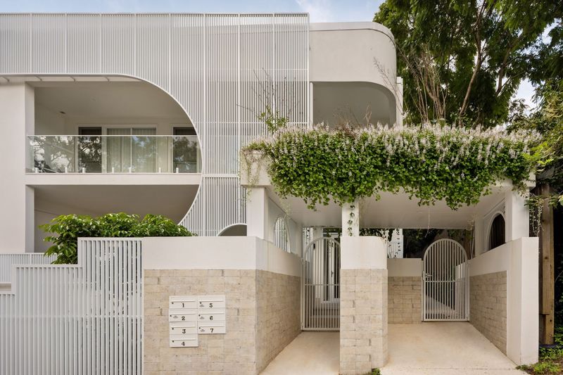 Entry to Ravine in Indooroopilly, curved white rendered walls, arched gates and a flowering vine over the entry