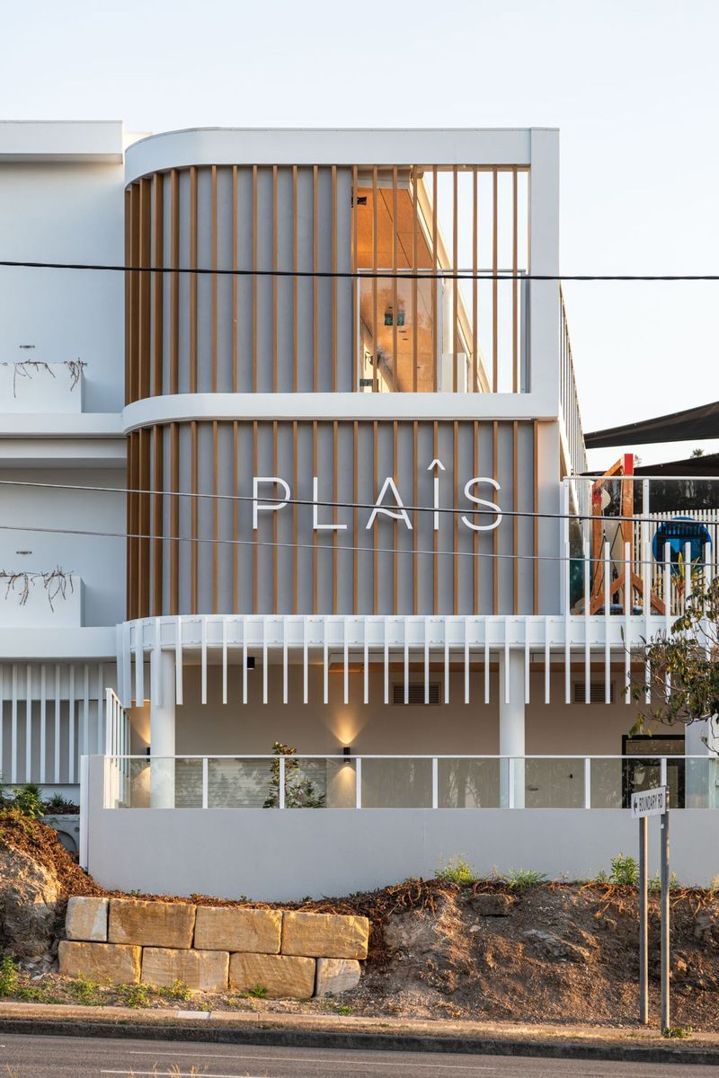 Curved corner of Plaîs Early Learning in Camp Hill with white rendered bands, vertical timber battens and the Plaîs sign